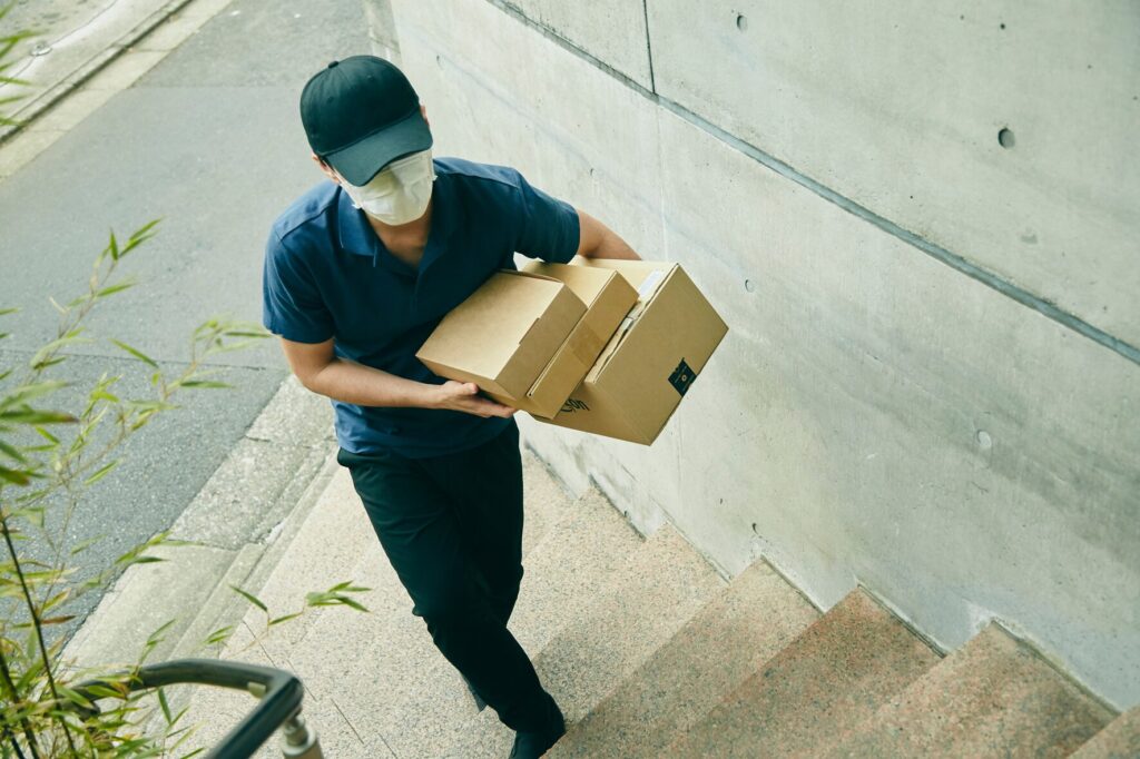複数の段ボール箱を抱えて階段を上る宅配ドライバー