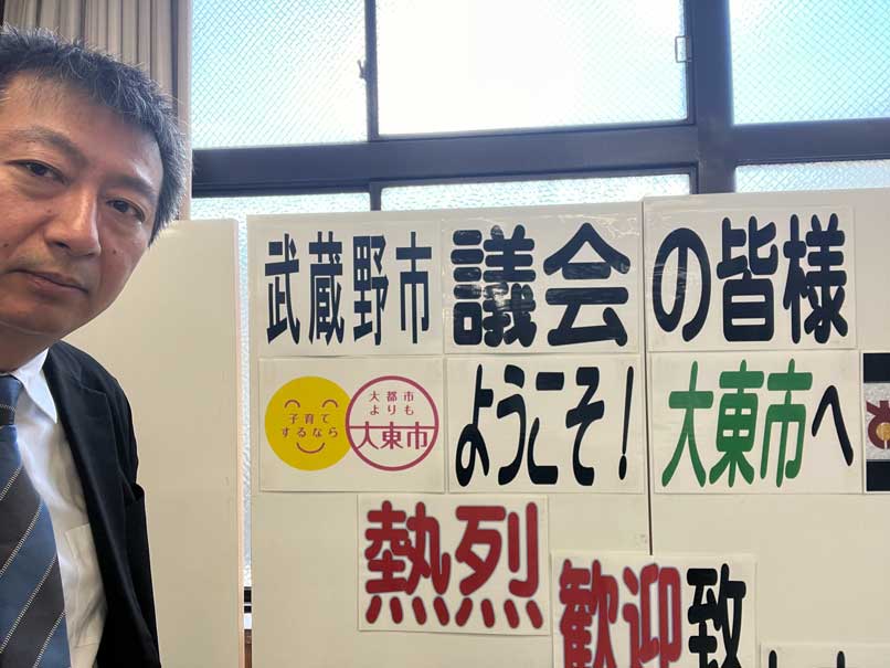 大東市で、武蔵野市議会の行政視察を歓迎する掲示の横に立つ藪原太郎